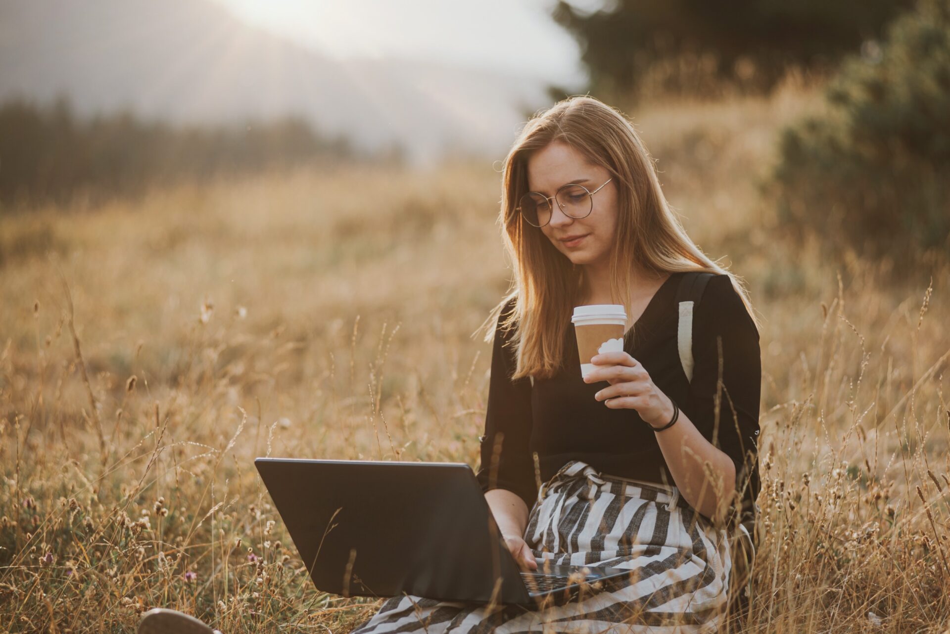 woman with glasses working on laptop while drinking coffee 